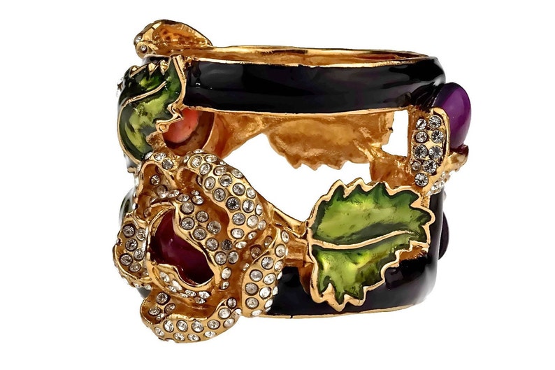 Puede incluir: Anillo de tono dorado con una banda de esmalte negro y un dise&ntilde;o floral tridimensional. La flor est&aacute; adornada con diamantes de imitaci&oacute;n transparentes y tiene un centro rojo y morado. El anillo tambi&eacute;n presenta hojas de esmalte verde.