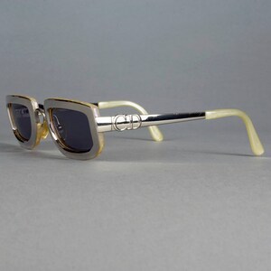 May include: Silver-toned sunglasses with a brown frame and dark lenses. The sunglasses have a 'CD' logo on the side.