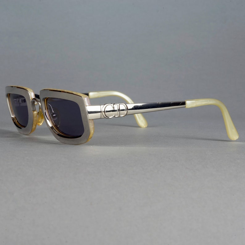 May include: Silver-toned sunglasses with a brown frame and dark lenses. The sunglasses have a 'CD' logo on the side.