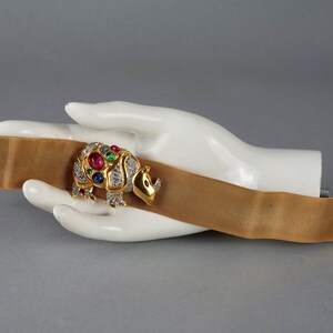 May include: A gold mesh bracelet with a jeweled rhinoceros charm. The charm is set with red, green, and blue gemstones and diamonds.