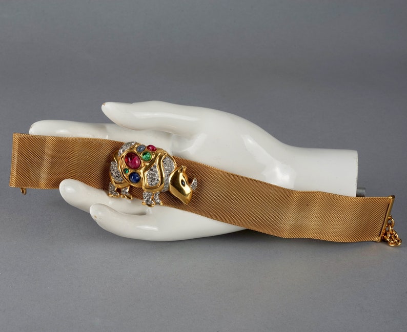 May include: A gold mesh bracelet with a jeweled rhinoceros charm. The charm is set with red, green, and blue gemstones and diamonds.