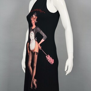 May include: Black sleeveless dress featuring a graphic of a woman in a maid outfit holding a pink feather duster. The text "Are You Feeling Dirty?" is printed above the graphic in red. The dress has a high neckline.