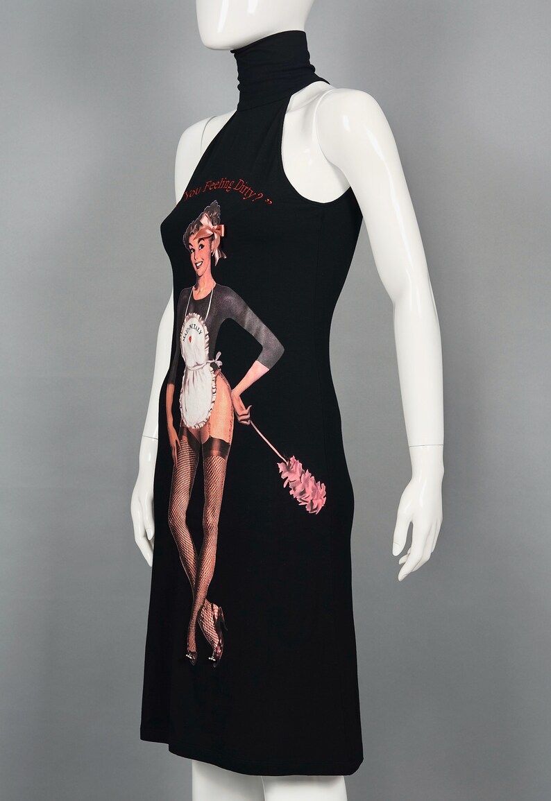 May include: Black sleeveless dress featuring a graphic of a woman in a maid outfit holding a pink feather duster. The text "Are You Feeling Dirty?" is printed above the graphic in red. The dress has a high neckline.