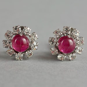 Może przedstawiać: Para srebrnych kolczyków z różowym kamieniem kaboszonowym otoczonym przez przezroczyste cyrkonie w kształcie kwiatu.