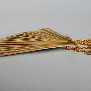May include: A gold-colored fan-shaped pendant necklace with a chain. The fan is made of multiple thin metal pieces that are connected together.