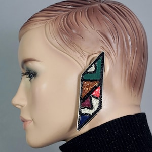 May include: A pair of large, geometric earrings with a black metal base and colorful, beaded designs. The earrings are shaped like a long, narrow triangle.