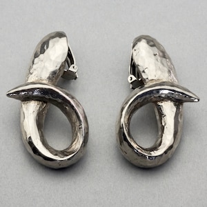 May include: A pair of silver clip-on earrings with a hammered texture and a twisted, knotted design.