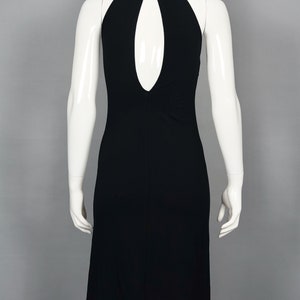 May include: A black halter dress with a keyhole back detail. The dress features a high neckline with three small buttons at the back. The dress is displayed on a white mannequin against a gray background.