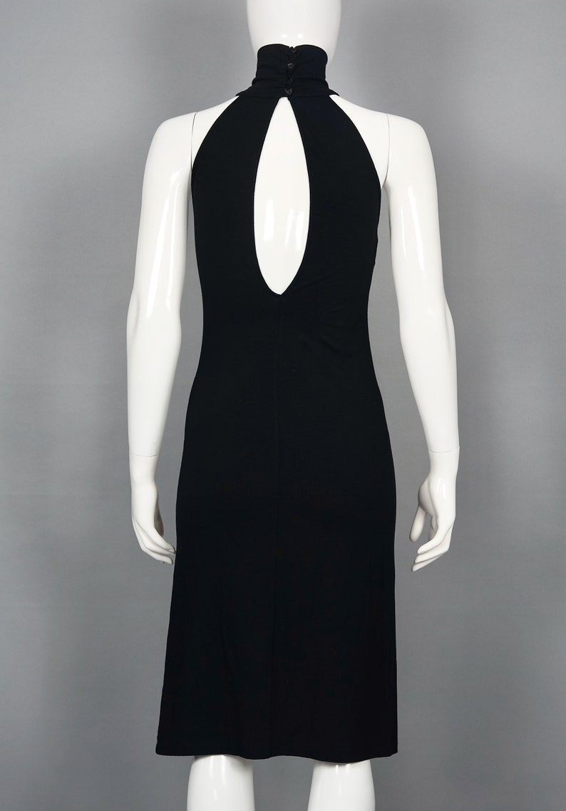 May include: A black halter dress with a keyhole back detail. The dress features a high neckline with three small buttons at the back. The dress is displayed on a white mannequin against a gray background.