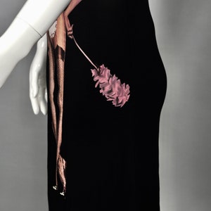 May include: Black dress featuring a pink floral design and a brown, snake-like pattern. The dress is displayed on a mannequin, showcasing its form and design. The dress has a unique, artistic aesthetic.