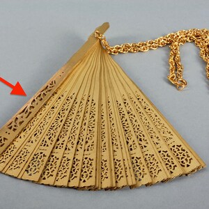 May include: A gold-colored fan with intricate cutouts and a gold chain attached. The fan is closed and folded.