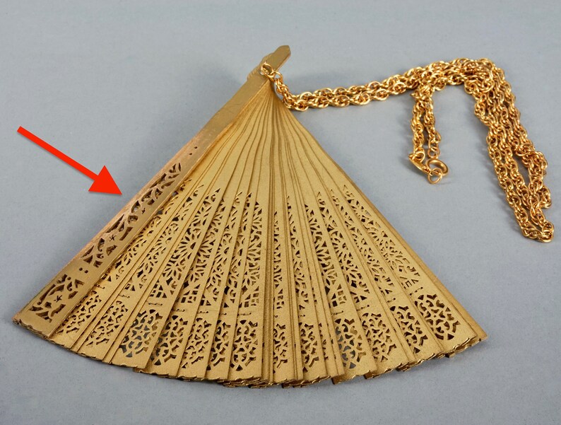 May include: A gold-colored fan with intricate cutouts and a gold chain attached. The fan is closed and folded.