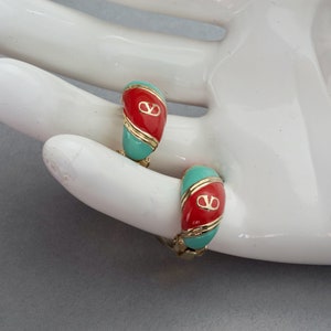 May include: A pair of gold hoop earrings with red and turquoise enamel. The earrings feature a gold logo in the center.