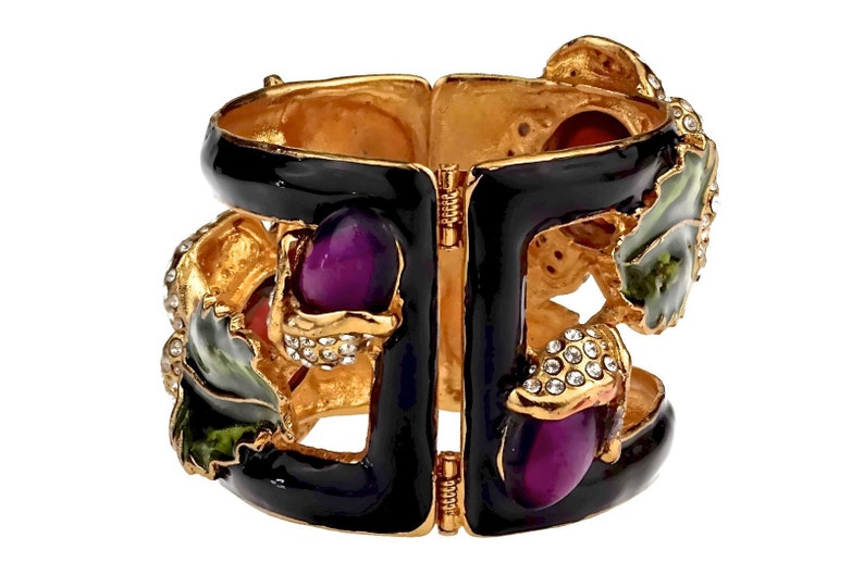 Puede incluir: Un brazalete de bisagra de esmalte negro con detalles dorados y detalles de esmalte de colores. El brazalete presenta un dise&ntilde;o floral con detalles de esmalte morado, verde y rojo. El brazalete est&aacute; adornado con pedrer&iacute;a transparente.