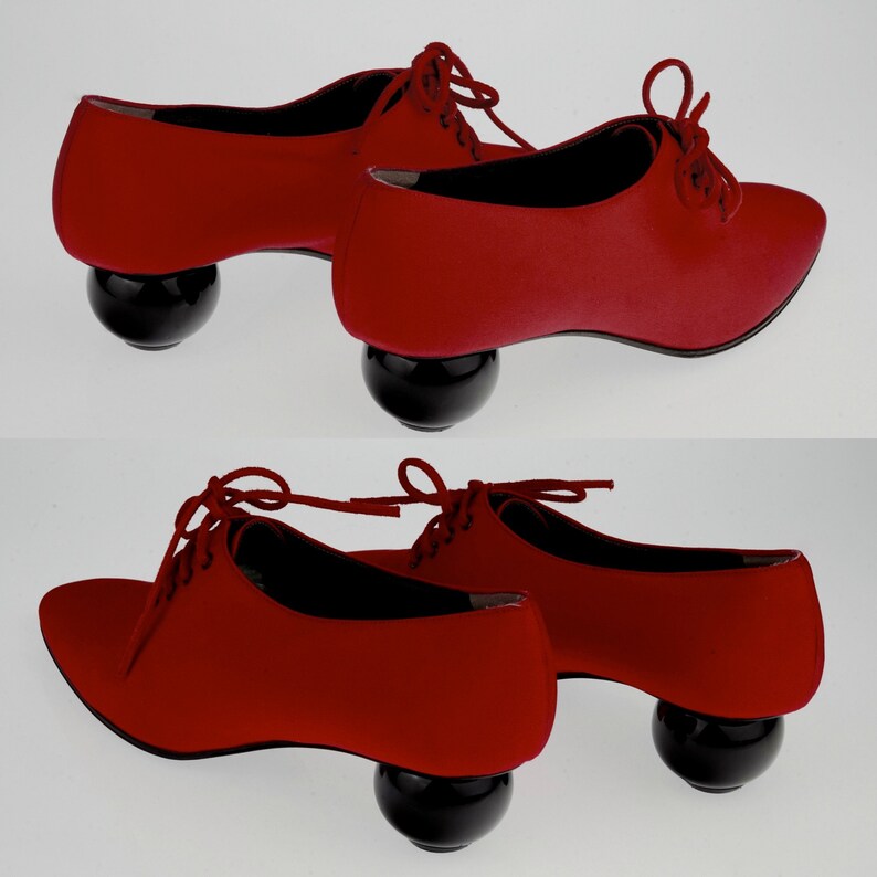 May include: Two pairs of red satin shoes with black ball-shaped heels. The shoes have lace-up fronts and are a unique and stylish design.