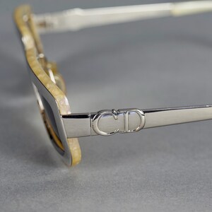 May include: Silver sunglasses with a white and yellow tortoiseshell frame. The sunglasses have a 'CD' logo on the side.