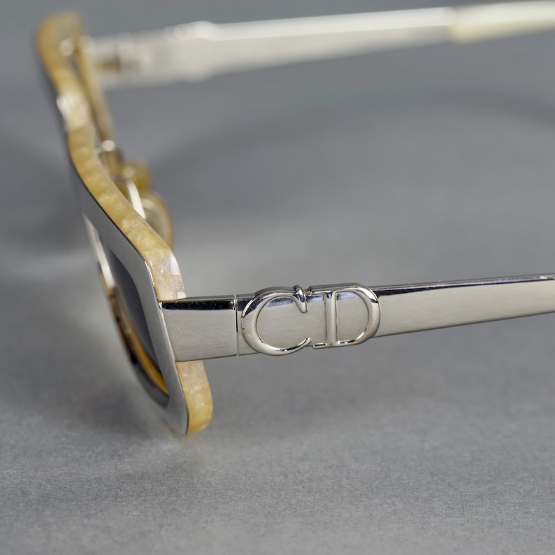 May include: Silver sunglasses with a white and yellow tortoiseshell frame. The sunglasses have a 'CD' logo on the side.