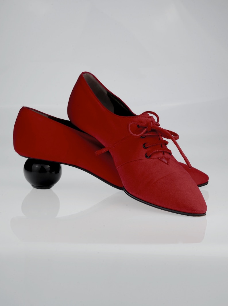 May include: A pair of red satin shoes with black laces and a round black heel.