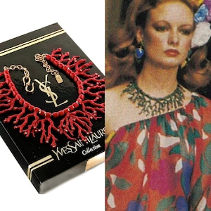 May include: A red coral necklace with a YSL logo on the box. The necklace is made of red coral branches and has a gold chain. The box is black with gold lettering. The necklace is part of the "Yves Saint Laurent Collection".