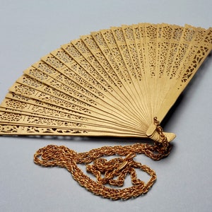 May include: A gold-colored, decorative fan with intricate cut-out designs. The fan is attached to a gold chain.