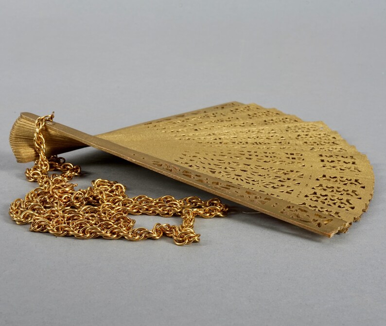 May include: A gold-colored metal fan pendant with a delicate, intricate design. The fan is attached to a gold chain.