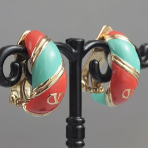 May include: A pair of red and turquoise clip-on earrings with gold accents. The earrings are shaped like a half-circle and have a logo on the front.
