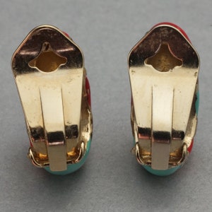 May include: A pair of gold-tone clip-on earrings with turquoise and red enamel. The earrings are shaped like a half-circle and have a simple design.