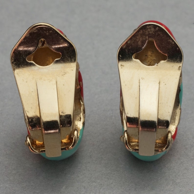 May include: A pair of gold-tone clip-on earrings with turquoise and red enamel. The earrings are shaped like a half-circle and have a simple design.