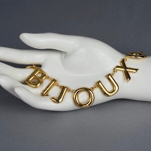 May include: A gold chain necklace with the word "BIJOUX" spelled out in large, chunky letters.