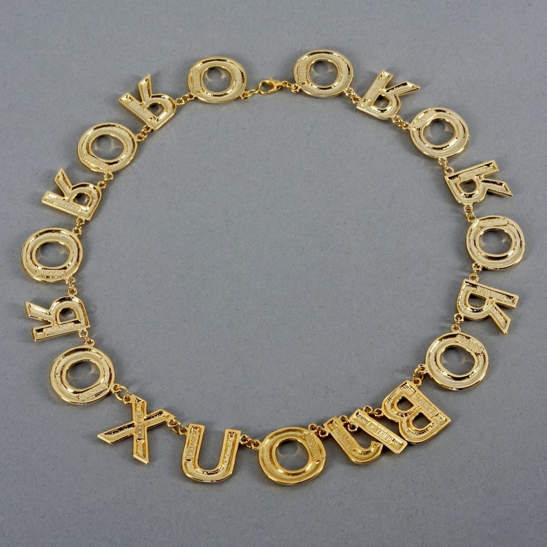 May include: A gold-tone necklace with letter charms spelling out "XOXO" and "YOU" in a circular design.