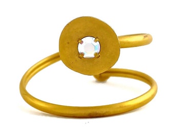 May include: A gold ring with a round, flat top featuring a clear iridescent stone.