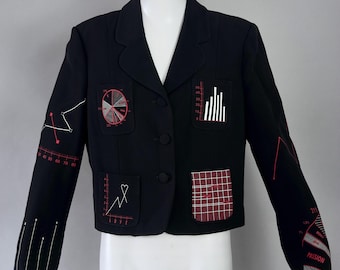 May include: Black blazer with unique embroidered designs. Features a pie chart, bar graph, and other geometric patterns in red and white. The blazer has a classic notched collar and two buttons.