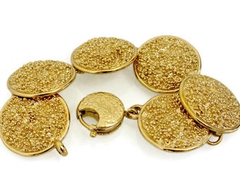 Puede incluir: Un brazalete de oro con un diseño circular texturizado. El brazalete tiene un cierre con un logotipo YSL.
