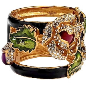 Puede incluir: Un brazalete de oro con base de esmalte negro y un gran dise&ntilde;o de rosa engastada. La rosa est&aacute; adornada con brillantes transparentes y una piedra central roja. El brazalete tambi&eacute;n presenta hojas de esmalte verde y bayas de esmalte morado.