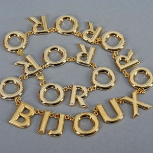 May include: A gold-tone necklace with the word "BIJOUX" spelled out in large letters, with the letters "OR" repeated throughout the necklace.