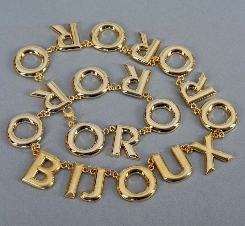May include: A gold-tone necklace with the word "BIJOUX" spelled out in large letters, with the letters "OR" repeated throughout the necklace.