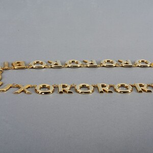 May include: A gold-tone necklace with a repeating pattern of the letter "O" and the letter "X".