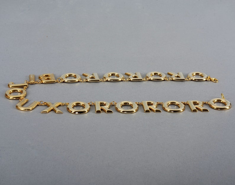 May include: A gold-tone necklace with a repeating pattern of the letter "O" and the letter "X".