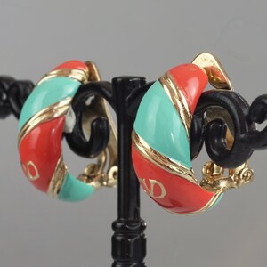 May include: A pair of gold tone clip-on earrings with a red and turquoise enamel design. The earrings are shaped like a half-circle and have a gold tone band around the edge.