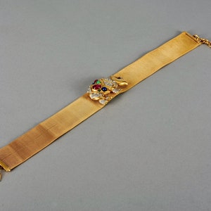 May include: A gold mesh bracelet with a jeweled frog charm. The frog is adorned with red, green, and blue gemstones.
