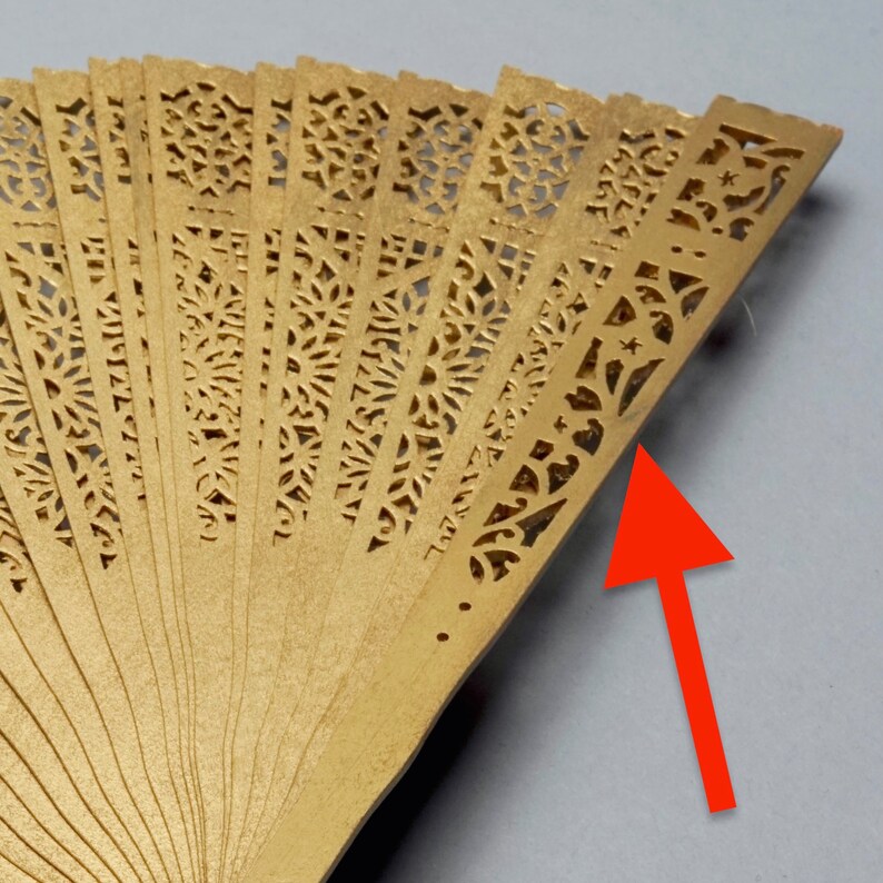 May include: A gold-colored folding fan with intricate cut-out designs. The fan is made of thin, delicate material and has a traditional Japanese style.