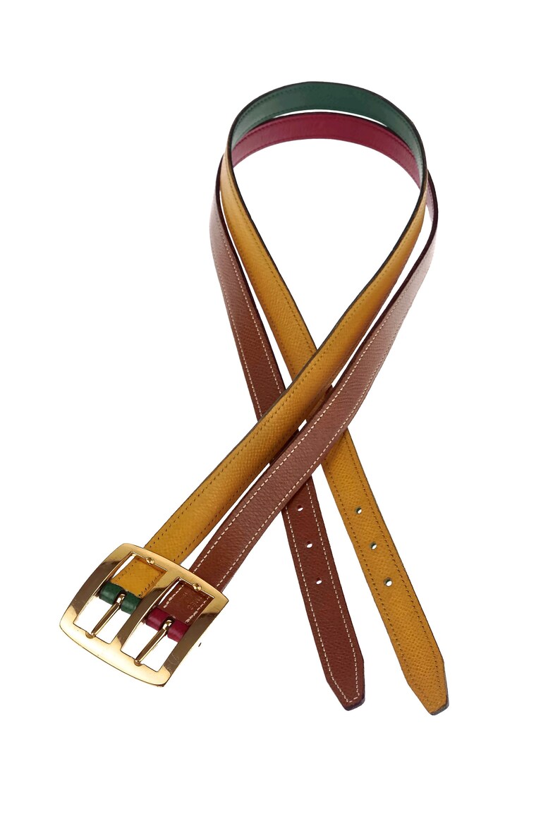 Pode incluir: Um cinto de couro revers&iacute;vel com uma fivela dourada. O cinto &eacute; marrom e amarelo de um lado e verde, vermelho e marrom do outro.
