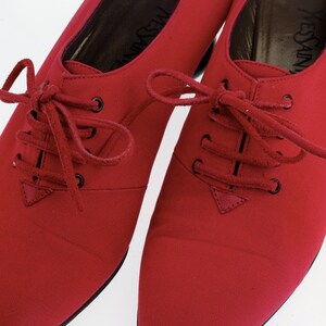 May include: A pair of red leather lace-up shoes with pointed toes. The shoes have a black leather sole and a black leather heel. The shoes are made by Yves Saint Laurent.