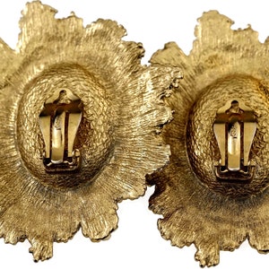 May include: A pair of gold-tone clip-on earrings with a floral design. The earrings are made of metal and have a textured finish.