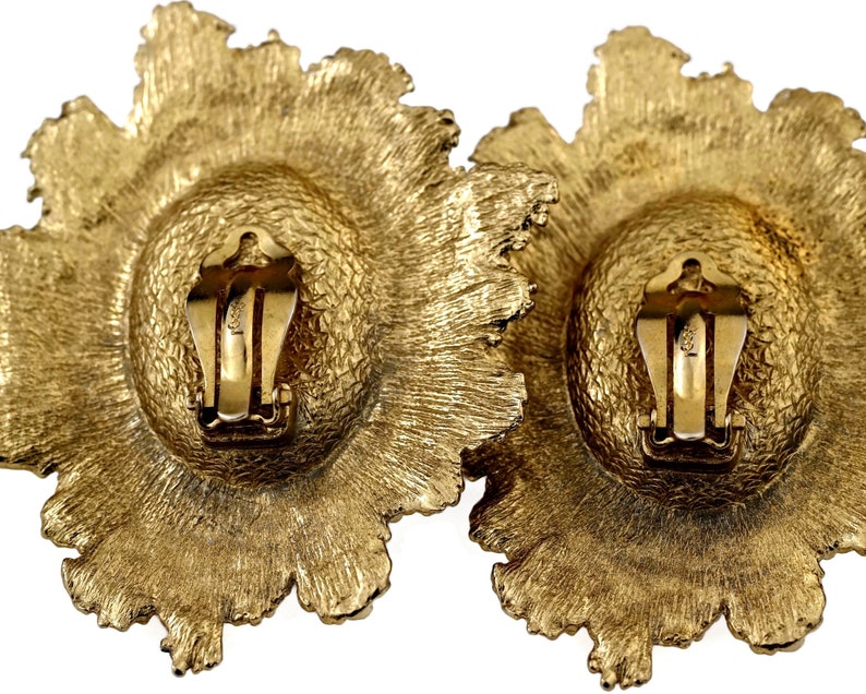 May include: A pair of gold-tone clip-on earrings with a floral design. The earrings are made of metal and have a textured finish.