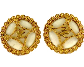 May include: A pair of gold earrings with a white pearl center and a gold filigree design. The earrings have a circular shape and are decorated with small gold beads.