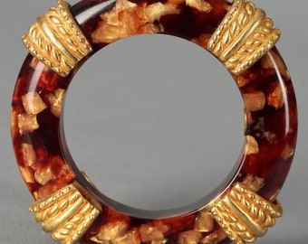 May include: A red and gold bangle bracelet with a textured, marbled design. The bracelet has gold accents on the sides.
