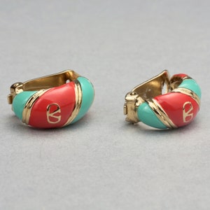 May include: A pair of gold-toned hoop earrings with red and turquoise enamel. The earrings feature a gold-toned logo in the center.