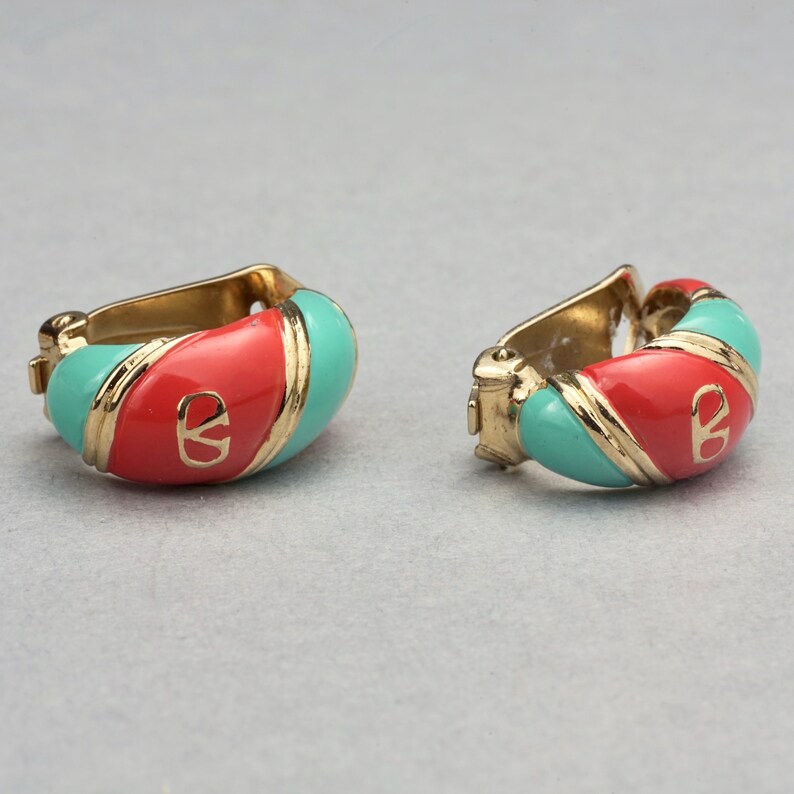 May include: A pair of gold-toned hoop earrings with red and turquoise enamel. The earrings feature a gold-toned logo in the center.