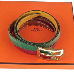 Pode incluir: Um cinto de couro multicolorido com uma fivela dourada. O cinto est&aacute; dobrado e apresentado numa caixa laranja com o logotipo da Hermes Paris.